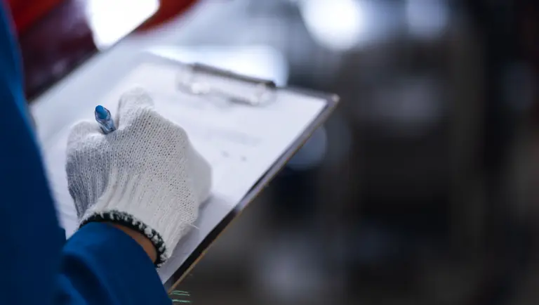 Iemand met beschermende handschoenen die een checklist of formulier invult op een klembord.